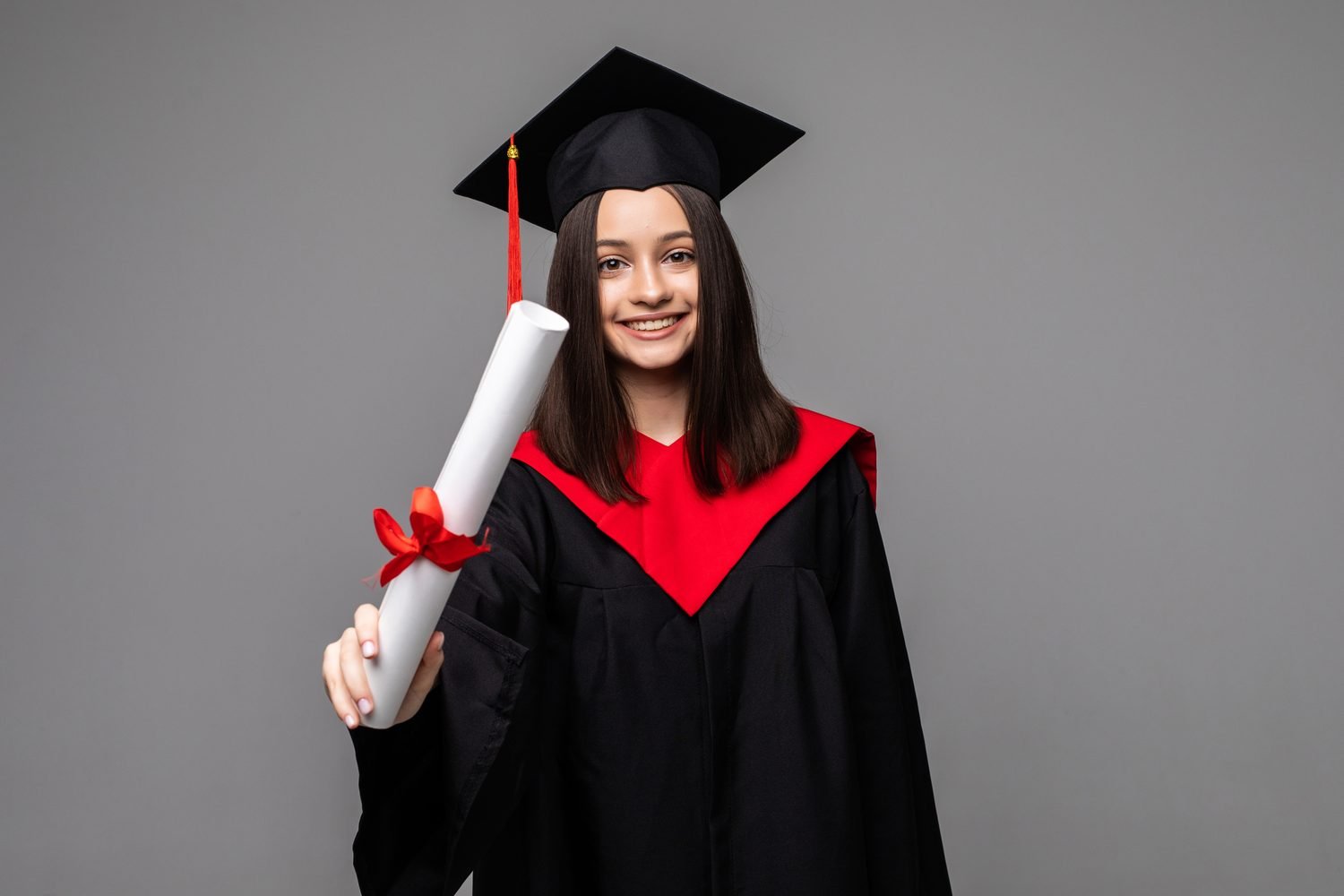 Graduada sonriendo y mostrando su diploma con listón rojo